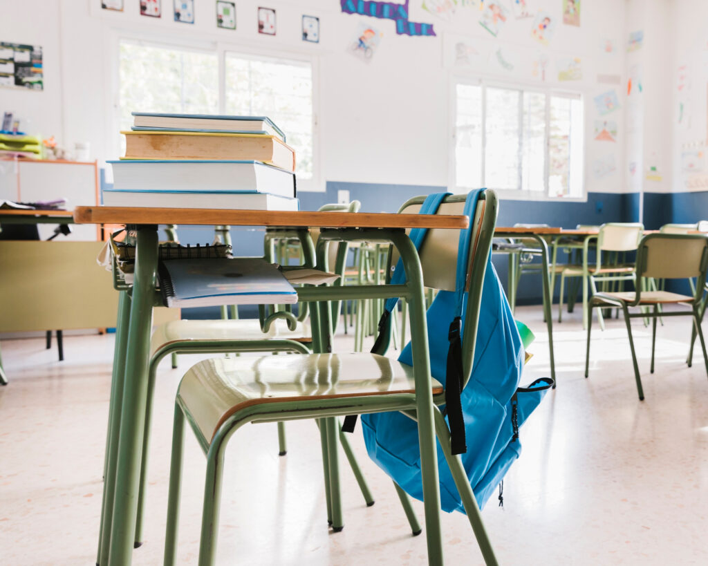 salle de classe avec une table en premier plan sur laquelle se trouve une pile de livre